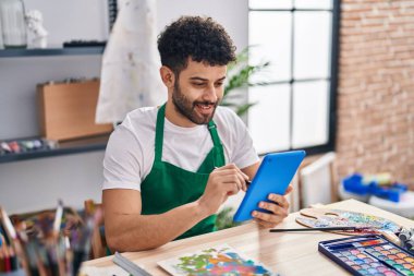 Genç Arap sanatçı, sanat stüdyosunda dokunmatik ped kullanarak gülümsüyor.