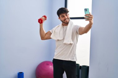 Elinde dambıl tutan genç bir İspanyol spor merkezinde akıllı telefondan selfie çekiyor.