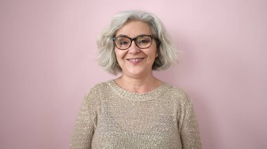 Middle age woman with grey hair smiling confident over isolated pink background