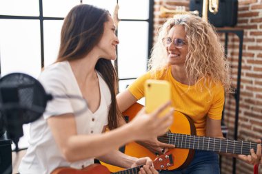 İki kadın müzisyen klasik gitar çalıyor ve ukulele müzik stüdyosunda akıllı telefon ekranı izliyor.