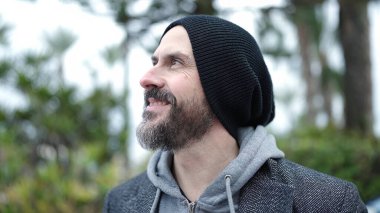 Genç kel adam parkın kenarına bakarak gülümsüyor.