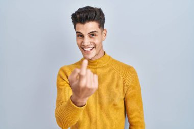 Young hispanic man standing over blue background beckoning come here gesture with hand inviting welcoming happy and smiling 