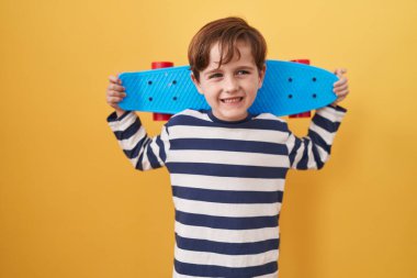 Küçük beyaz çocuk sarı arka planda paten kayıyor çılgınlığı kutluyor ve başarıyı hayretle haykırıyor.. 