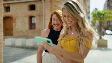 İki kadın birlikte caddede akıllı telefondan video izliyorlar.