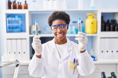 African american woman wearing scientist uniform holding test tubes at laboratory