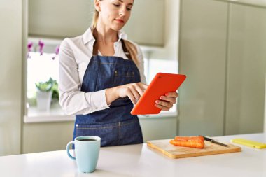 Genç sarışın kadın mutfakta dokunmatik ped kullanıyor.