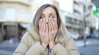 Young blonde woman standing with surprise expression at street