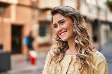 Gülümseyen genç bir kadın sokağın kenarına bakıyor kendinden emin.