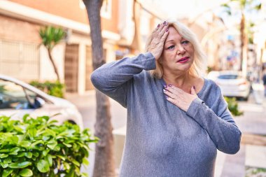 Middle age blonde woman with headache at street