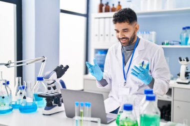 Young hispanic man wearing scientist uniform having video call at laboratory