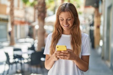 Young blonde girl smiling confident using smartphone at street