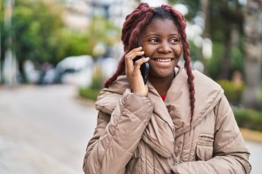Afro-Amerikalı kadın gülümsüyor. Akıllı telefondan konuşuyor.