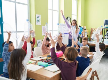 Geri dönüşüm dersi alan kadın ve çocuklar sınıfta boş şişe tutuyorlar.