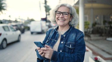 Middle age woman with grey hair using smartphone at street