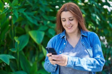 Young beautiful plus size woman smiling confident using smartphone at park