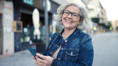 Middle age woman with grey hair using smartphone at street