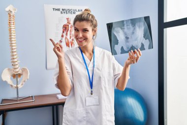 Elinde leğen kemiği radyografisi olan genç bir kadın gülümsüyor. 