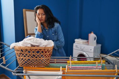 Çamaşır ipine elbise asan genç Asyalı kadın kollarını kavuşturup depresyondan sıkılmış ve yorgun göründüğünü düşünüyor.. 