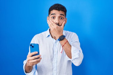 Akıllı telefondan mesaj yazan sakallı İspanyol adam ağzını yanlışlıkla elleriyle kapatarak şok etti. gizli kavram. 