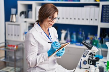 Laboratuvarda not defterine yazan orta yaşlı kadın bilim adamı.