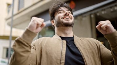 Genç İspanyol adam gülümsüyor. Kendine güveni tam. Kazanan yüz ifadesiyle sokakta duruyor.