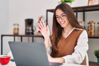 Genç, güzel, İspanyol bir kadın evdeki masada oturmuş video görüşmesi yapıyor.