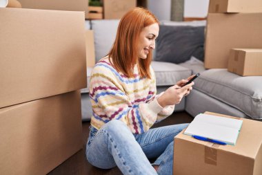 Young caucasian woman using smartphone sitting on floor at new home