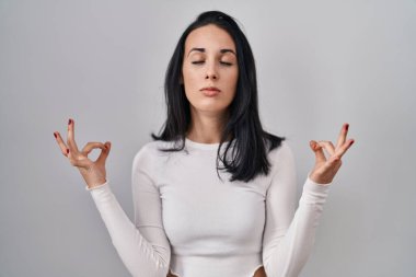 Tecrit edilmiş arka planda duran İspanyol kadın rahatla ve gözleri kapalı gülümse parmaklarıyla meditasyon hareketi yapıyor. yoga konsepti. 