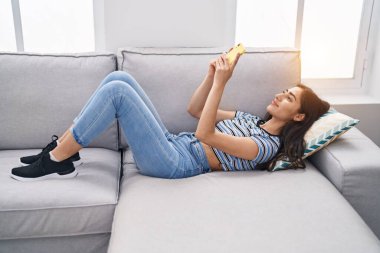 Evdeki kanepede uzanmış akıllı telefon kullanan genç İspanyol kız.