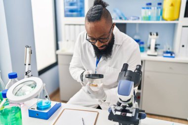 Genç Afrikalı Amerikalı adam bilim adamı üniforması giyiyor. Laboratuvarda Loupe 'u kullanıyor.