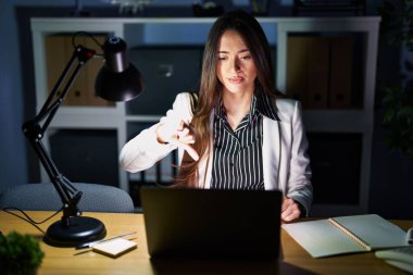 Genç esmer kadın geceleri ofiste dizüstü bilgisayarla çalışıyor mutsuz ve sinirli görünüyor reddediliyor ve olumsuz bir hareket yapıyor. kötü ifade. 