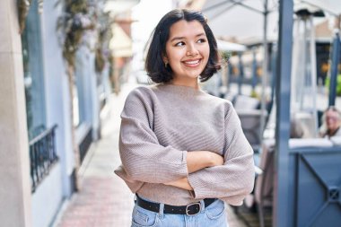 Young woman standing with arms crossed gesture looking to the side at street