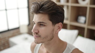 Young hispanic man sitting on bed with relaxed expression at bedroom