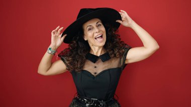 Middle age hispanic woman wearing witch costume having halloween party over isolated red background