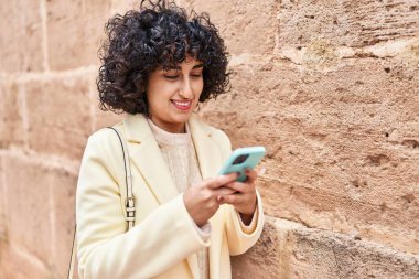 Orta Doğulu genç kadın güler yüzlü, kendine güler yüzlü, akıllı telefon kullanıyor.