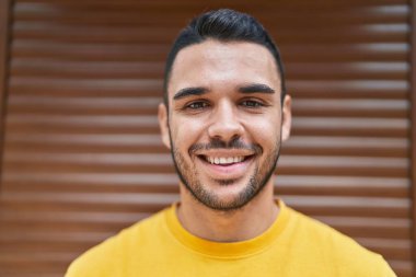 İzole edilmiş kahverengi arka planda duran kendine güvenen İspanyol genç adam.