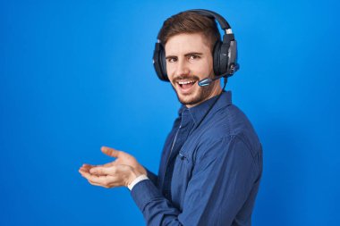 Sakallı, müzik dinleyen, kulaklık takan, avuç içi açık, fotokopi alanını gösteren, gülümseyen mutlu bir gülümseme sunan İspanyol bir adam. 