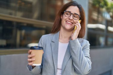 Genç iş kadını akıllı telefondan konuşuyor. Sokakta kahve içiyor.