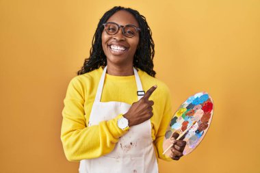 Afrikalı bir kadın ressam paleti tutuyor. Neşeli, yüzünde bir gülümseme var. Yüzünde mutlu ve doğal bir ifade var. 