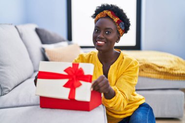 Young african american woman unboxing present package sitting on floor at home