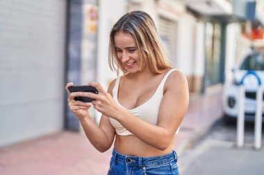 Sokakta video oyunu oynarken kendine güvenen genç sarışın kadın.