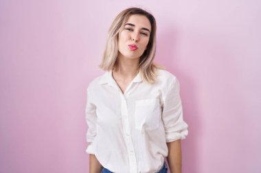 Genç ve güzel bir kadın pembe arka planda dikilip kameraya bakıyor ve güzel ve seksi bir şekilde yayına öpücük yolluyor. aşk ifadesi. 