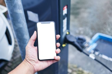 Man holding smartphone showing white blank screen at electrical car station