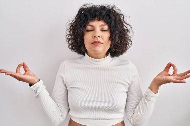 Kıvırcık saçlı İspanyol kadın izole edilmiş arka planda durup rahatlamış ve gözleri kapalı parmaklarıyla meditasyon hareketi yaparken gülümsüyor. yoga konsepti. 