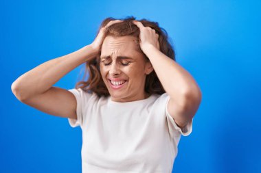 Genç, güzel, İspanyol bir kadın baş ağrısı çekiyor ve mavi arka planda ağlıyor.