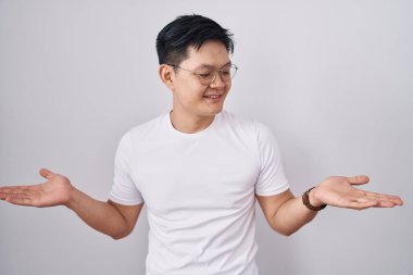 Beyaz arka planda duran Asyalı genç adam gülümseyerek avuçlarını açık gösteriyor, karşılaştırma ve reklam karşılaştırması yapıyor ve dengeyi sağlıyor. 