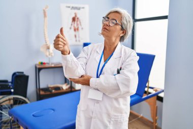 Beyaz saçlı orta yaşlı bir kadın ağrı kesici kliniğinde çalışıyor. Gururlu görünüyor, gülümsüyor. Kenarda baş parmak hareketi yapıyor. 