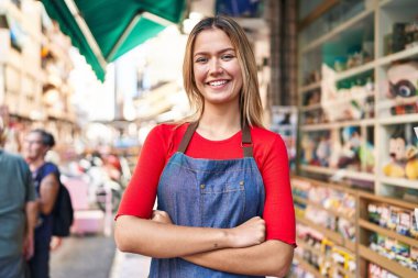 Young hispanic woman shop assistant standing with arms crossed gesture at street