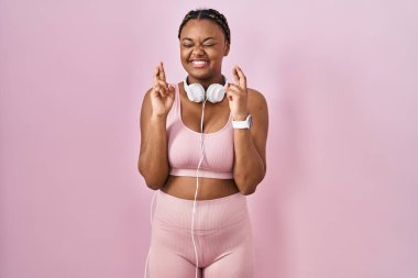 Spor kıyafetleri ve kulaklıkları takan Afro-Amerikan kadın umut ve gözleri kapalı bir şekilde gülümseyerek el sallıyor. Şans ve batıl inançlar. 