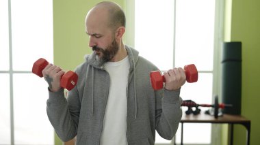 Spor merkezinde halterleri kullanarak gülümseyen kel bir genç.